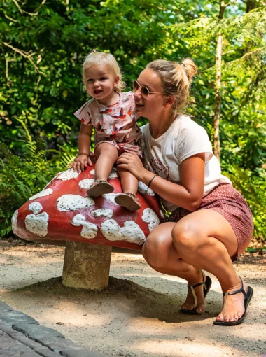 Marissa en Nina zitten bij een kleurrijke paddenstoel in het Sprookjesbos van de Efteling, genietend van de sprookjesachtige sfeer.