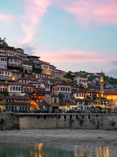 Berat, Albanië, bij zonsondergang met kleurrijke hemel en de verlichte huizen van de stad.