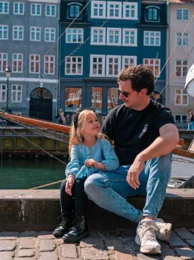 Vader en dochter zitten op de kade van Nyhavn, een leuke plek om met kinderen te bezoeken in Kopenhagen.